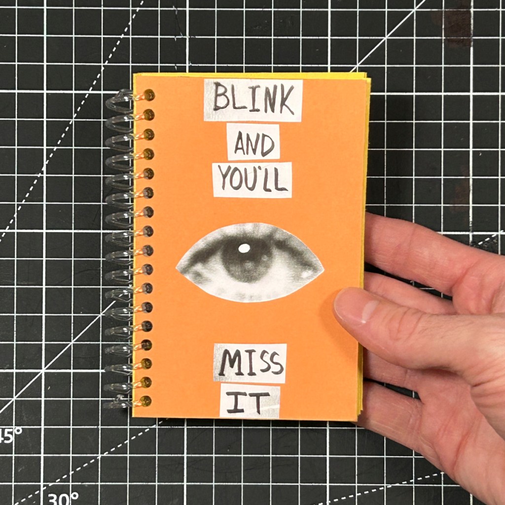 Blink and You’ll Miss It, an orange spiral-bound photo zine by Sullivan Sweet, held over a black gridded cutting mat.